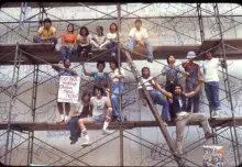 young people sitting on scaffolding while painting mural 